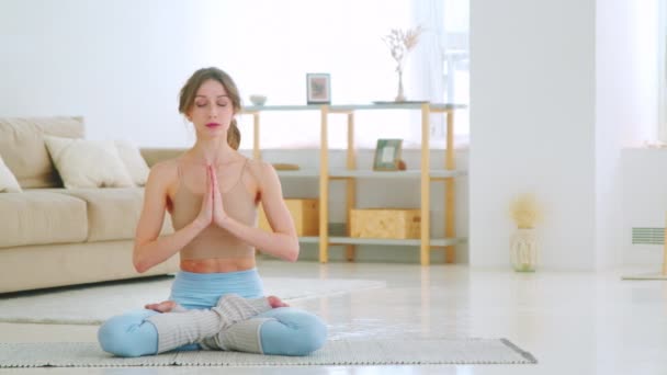 Entspannte Frau in Sportbekleidung meditiert in Lotusposition sitzend auf Yogamatte mit den Händen im Gesicht — Stockvideo
