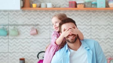 Küçük bir kız elleriyle babasının gözlerini kapatıyor. Baba ve kızı birlikte vakit geçiriyorlar.
