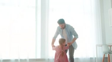 Genç bir baba, evin içinde uçan bir kızı tutuyor. Mutlu bir aile.