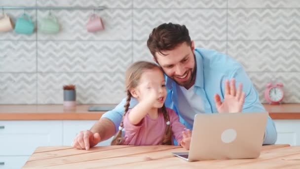 Padre joven e hija pequeña hablando en una conferencia en línea con mamá usando una computadora portátil. Familia joven con un niño — Vídeo de stock
