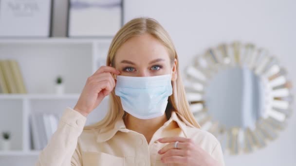 Rapariga a tirar a máscara médica azul. Jovem sorrindo mulher tirando sua máscara dentro de casa — Vídeo de Stock