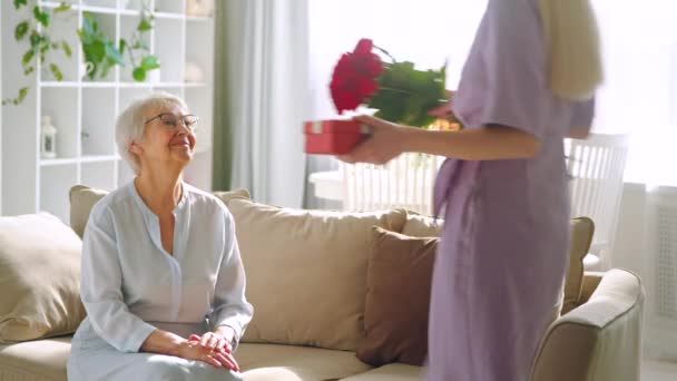 Giovane donna che fa un regalo alla sua anziana madre in un interno della casa. Buon compleanno. — Video Stock