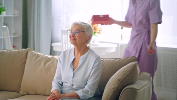 Dlouhé vlasy blondýny v purpurových šatech dává malou krabičku s dárkem pro starší dámu s radostným úsměvem — Stock video