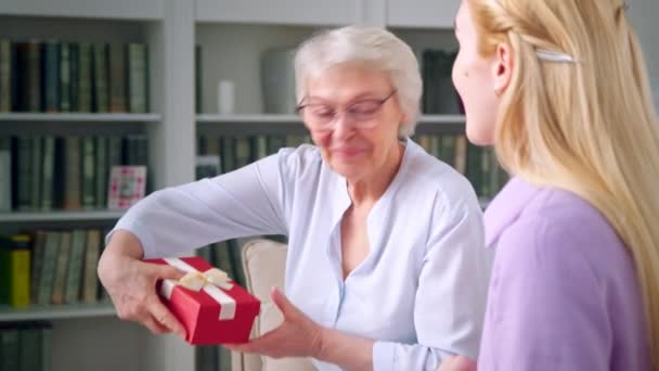 Oudere moeder met bril geven een geschenk aan een jonge dochter thuis — Stockvideo