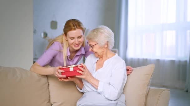 Jonge dochter geeft een cadeau aan een oudere moeder thuis — Stockvideo