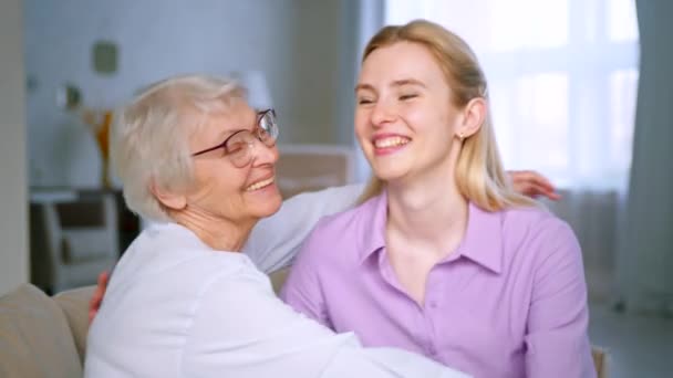 Chica joven y anciana abrazando y mirando a la cámara. Familia feliz en casa — Vídeo de stock