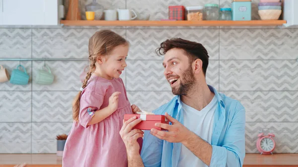 Menina bonito dando um presente para o pai para umas férias na sala de estar. Um dos pais com um filho em casa — Fotografia de Stock