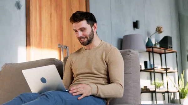 Hombre sonriente con portátil en el trabajo sentado en el sofá —  Fotos de Stock