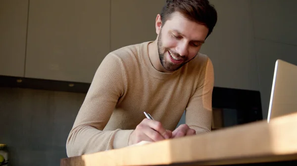 Jongeman maakt notities in de keuken — Stockfoto