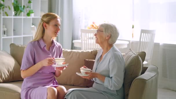 Praten jong meisje en oudere moeder met kopjes thee thuis. Levensstijl concept — Stockvideo