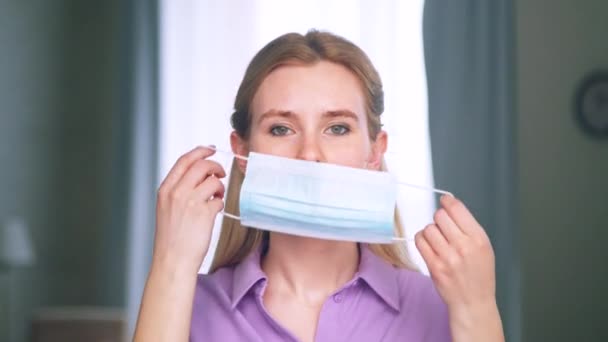 Молодая девушка надевает синюю медицинскую маску в квартире — стоковое видео