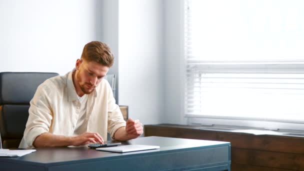 Thoughtful manager with beard sums up expenses on calculator — Stock Video