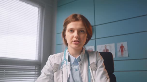 Brunette medical worker in white coat talks on video call — Stockvideo