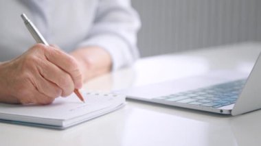 Old lady wrinkly hand holds grey brown pen and writes notes
