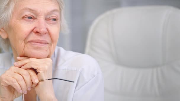 Mulher envelhecida com cabelo curto olha para a janela segurando óculos — Vídeo de Stock