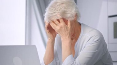 Depressed lady pensioner massages temples sitting at table