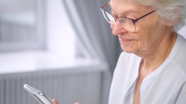 Delighted senior woman with glasses types on smartphone