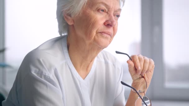 Grey haired old lady in white blouse holds glasses in hand — Stock Video