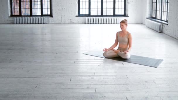 Slim praticante di yoga si siede su stuoia meditando in studio — Video Stock