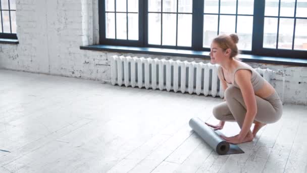 Mulher alegre desenrola tapete de borracha antes de treinar em estúdio — Vídeo de Stock