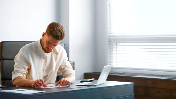 Bearded guy manager in geel shirt sorteert papieren ontvangstbewijzen — Stockvideo