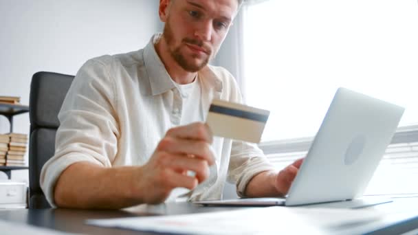 Bearded company manager types yellow card number on laptop — Αρχείο Βίντεο