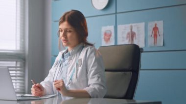 Genç kadın doktor hastaya kağıtlara bakarak konuşuyor.