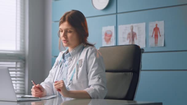 Молодая женщина врач разговаривает с пациентом глядя на документы — стоковое видео