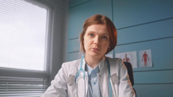 Rödhårig dam allmänläkare pratar med patienter — Stockvideo
