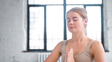 Güzel bir kadın namaste Mudra 'da el ele tutuşurken derin bir nefes alır.