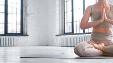 Nilüfer çiçeği pozunda meditasyon yapan bir kadın stüdyoda yerde oturuyor.