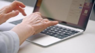 Yaşlı kadın elleri gri dizüstü bilgisayarın siyah klavyesini kullanıyor.