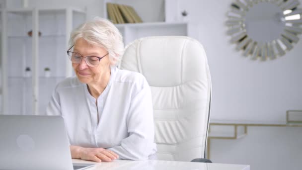 Aged businesswoman with glasses looks into laptop display — Stok Video