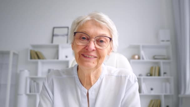 Lächelnde grauhaarige Mutter mit Brille winkt mit der Hand zum Gruß — Stockvideo