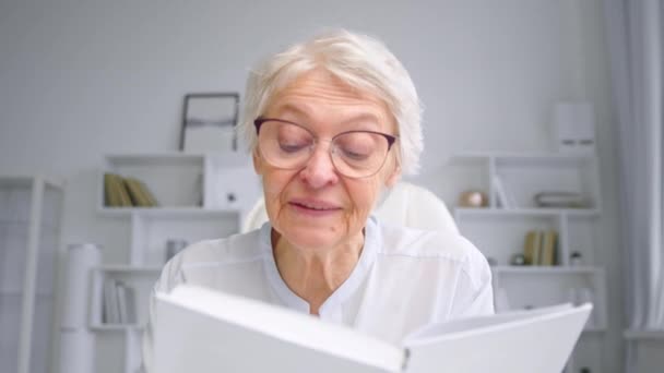 Old manager läser bok sittande på online videokonferens — Stockvideo