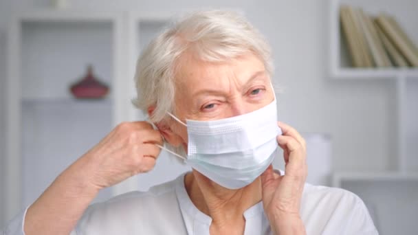 Mujer mayor con pelo gris se quita la mascarilla blanca — Vídeos de Stock