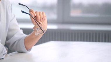 Thoughtful old businesswoman hand holds glasses over table