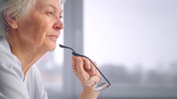 Thoughtful aged woman in blue blouse holds designed glasses — Stock Video