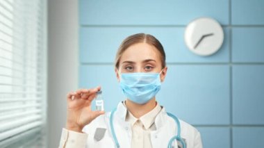 Young woman doctor holds large vial and looks straight