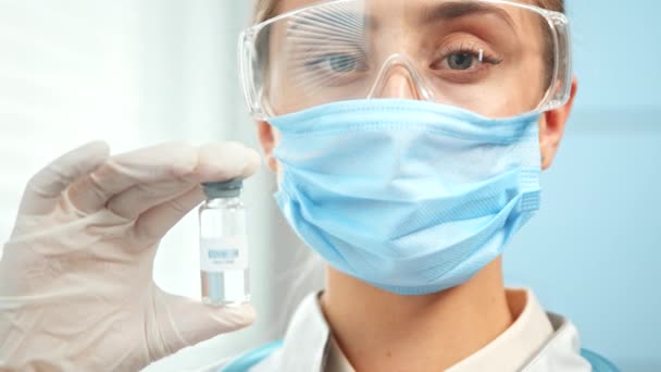 นักวิจัยหญิงในหน้ากากและแว่นตาถือขวดวัคซีน — วีดีโอสต็อก