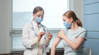 Sarışın kadın hastane hemşiresi genç bayana iğne yapıyor.