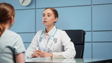 Beyaz önlüklü genç bayan doktor hastane ziyaretçisini muayene ediyor.