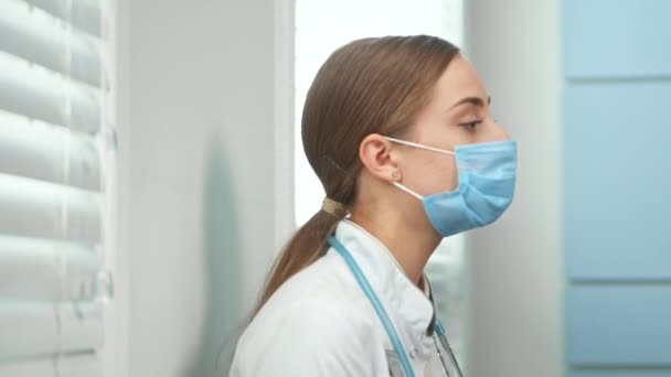 Mujer joven agotada con abrigo blanco se quita la máscara médica — Vídeo de stock
