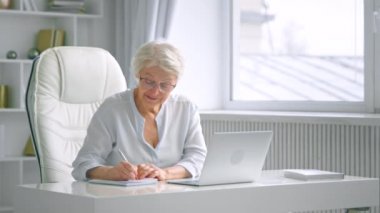 Gri saçlı bayan dizüstü bilgisayarla konuşur not alır