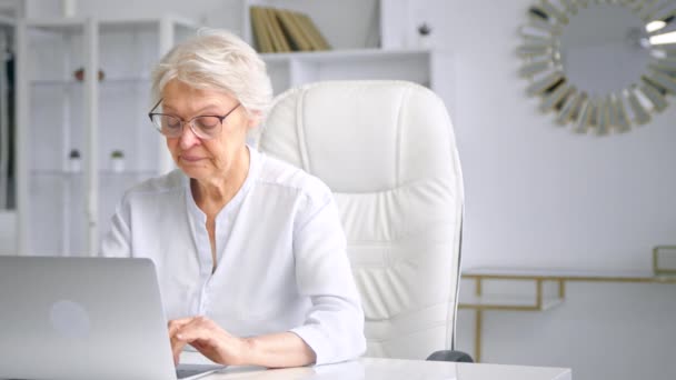 Gerente de señora de edad concentrada en tipos de gafas en el ordenador portátil — Vídeos de Stock