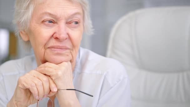 A nyugdíjas hölgy szemüveggel tartja a fejét a kezén. — Stock videók