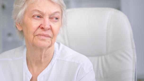 Old mother with wrinkly face and sad blue eyes looks aside — Stock Video