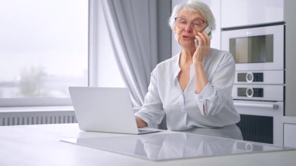 Mujer de negocios mira a la computadora portátil y habla en el teléfono inteligente — Vídeos de Stock