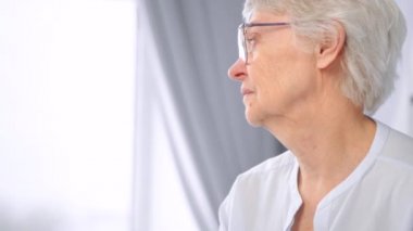 Kısa gri saçlı ve gözlüklü düşünceli yaşlı kadın.