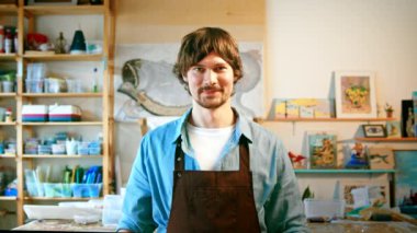 Önlüklü, gülümseyen olgun bir adam kameraya bakıyor.